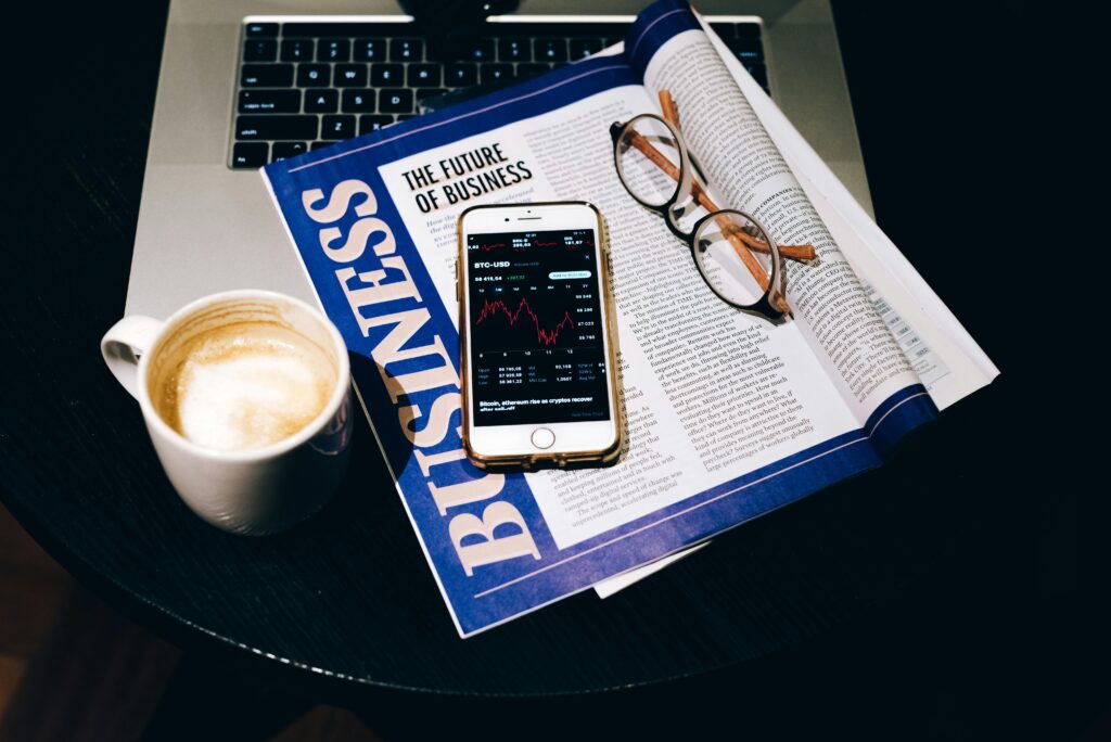 A business setup with a laptop, coffee, phone, and newspaper. Perfect for finance themes.
